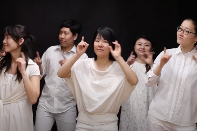 Five Japanese people dressed in white clothing signing along music