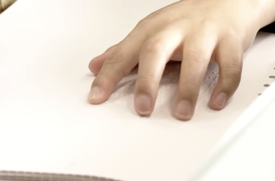a close up of a young Japanese child's hand moving over braille text