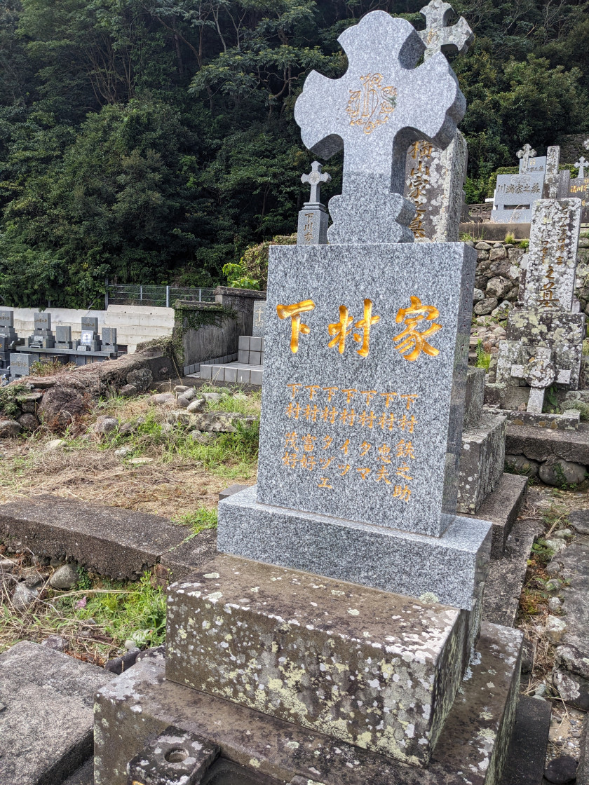 Photograph of a Catholic grave with the family name Shimomura written in gold kanji.