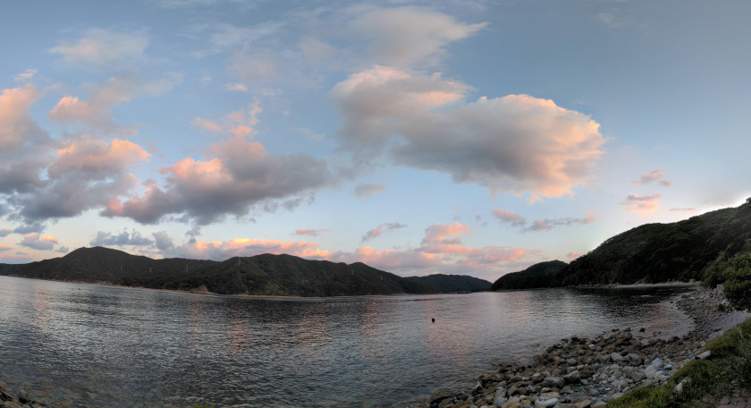 A photograph of the view from Hidden Kirishitan Resource Center, a sunset over small mountains with a placid body of water in front.