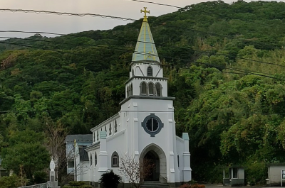 Photograph of the Hamawaki Church, a green roofed, white colored church against green forest background.