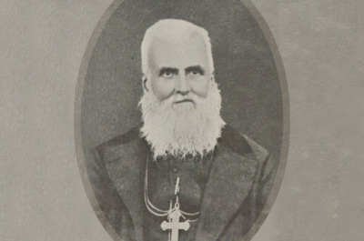 Photograph portrait of Jule-Alphonse Cousin. A senior Caucasian Catholic priest with long white beard in jacket with cross necklace.