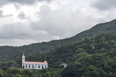 A photograph of red roofed church building in the middle of a mountainside full of trees.