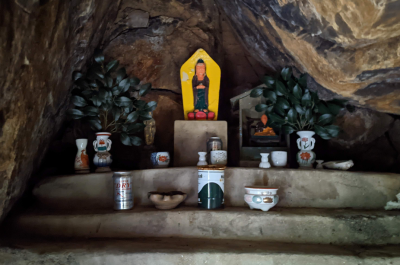 A photograph of a small memorial site under a stone awning with offerings in front of it.