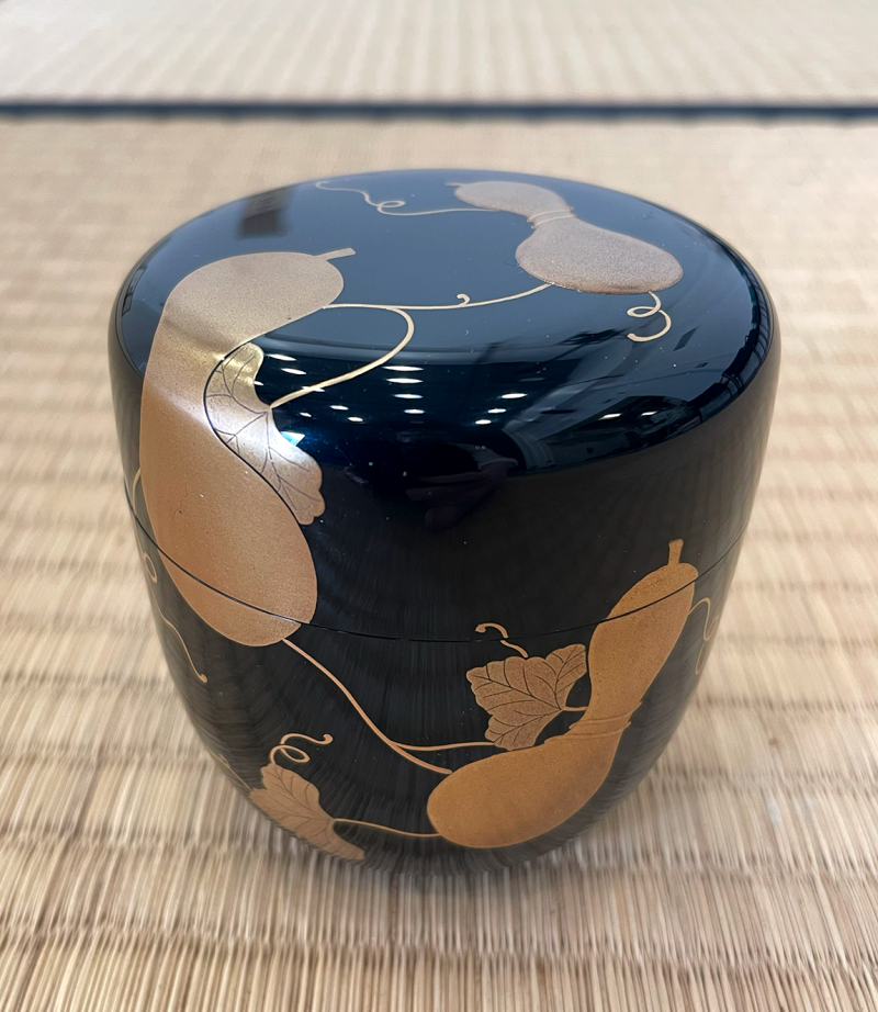 A small black lacquered container with gold decorations of gourds.