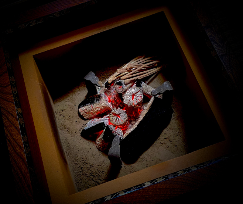 A pile of gray and brown charcoal, glowing black and red in between the pieces, sitting in a pile of ashes inside a rectangular brazier container.