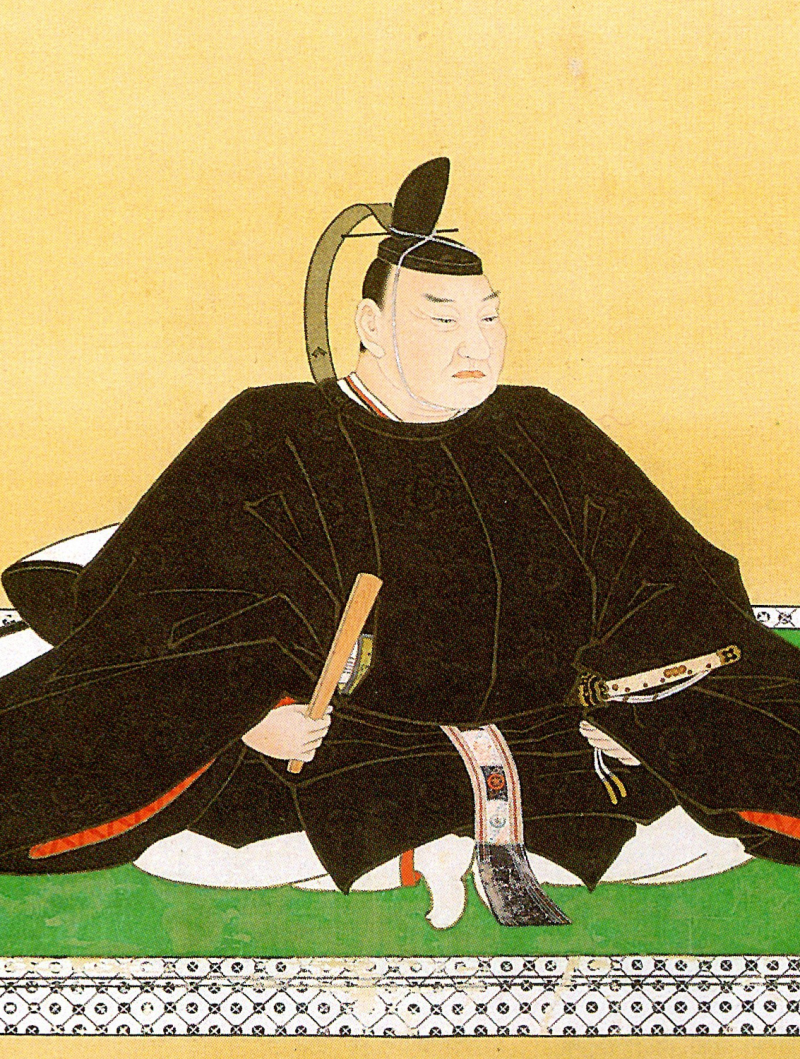 A sturdy man dressed in formal black warrior clothes and courtier cap, holding a fan and with a sword at his side.