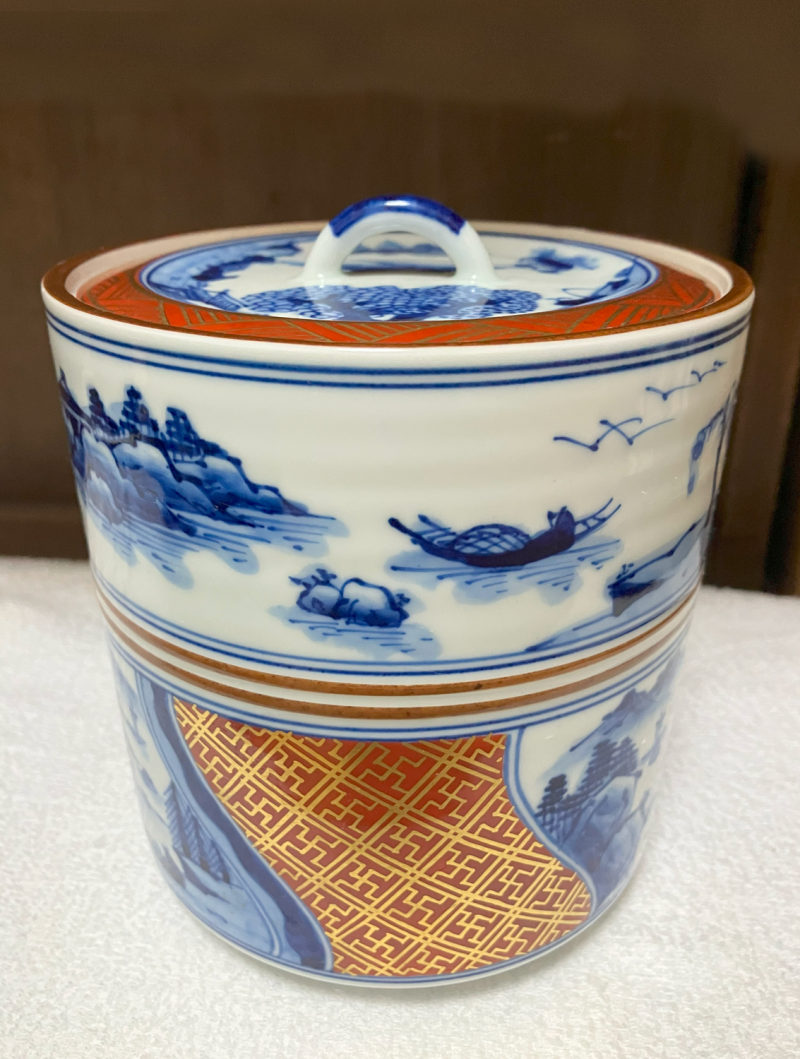 Porcelain cold water container with matched porcelain lid. The pattern is classic blue and white pictures of Chinese water and mountain scapes with red and gold accent panels.