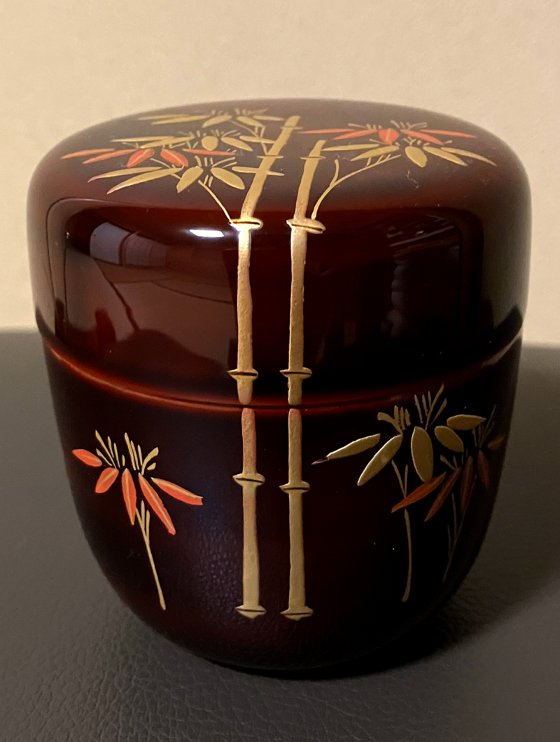 Wine-brown laquer natsume with a painted gold and orange pattern of bamboo that reaches from bottom to lid.