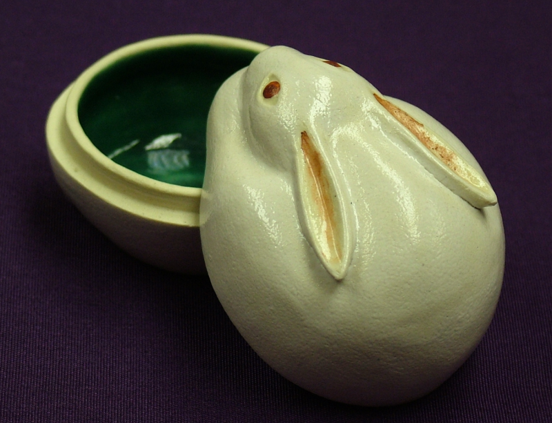 Small ceramic incense container in the shape of a white rabbit with red eyes and relief ears. The lid is ajar, revealing a green glazed interior.