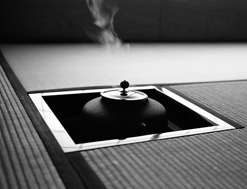 Square wood frame among tatami reed woven mats with the top of the iron kettle rising slightly above the level of the floor.