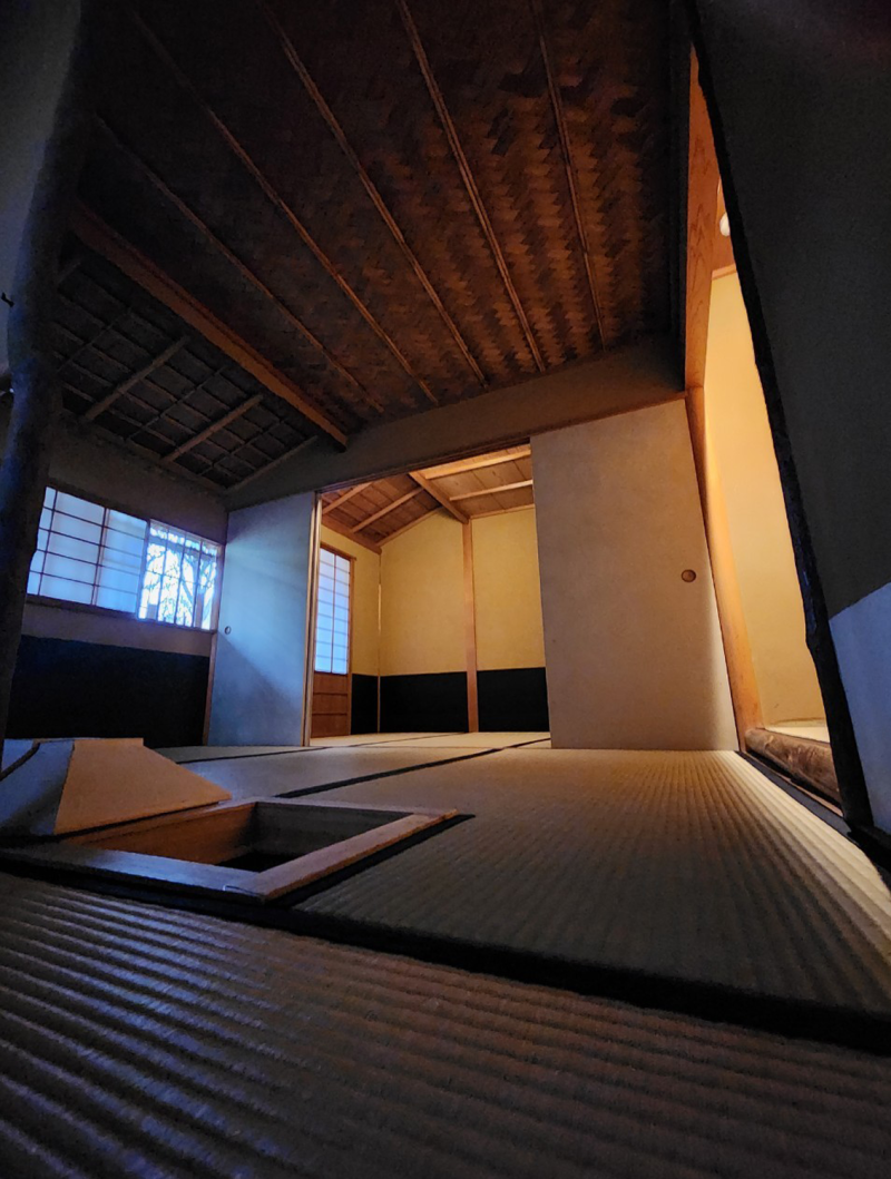 An interior view of the tearoom looking over and up from the floor to show the woven matting of the ceiling in the center of the room and a cross bar patern of narrow wooden polls on one outer edge of the room.