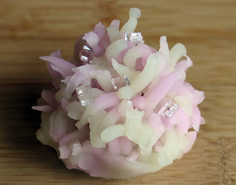 A closeup of a hydrangea tea sweet, which is light pink and white with little clear cubes. The sweet is designed to look like petals of the flower clustered.